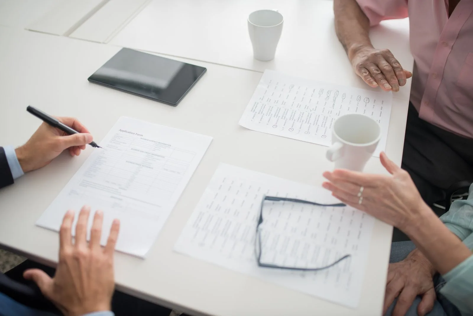 Haftung bei Schäden durch die Reinigungsfirma: was Hausverwaltungen klären sollten Weißer Besprechungstisch mit Formularen, einem Stift, Tablet und Kaffeetassen, daran sitzen mehrere Personen