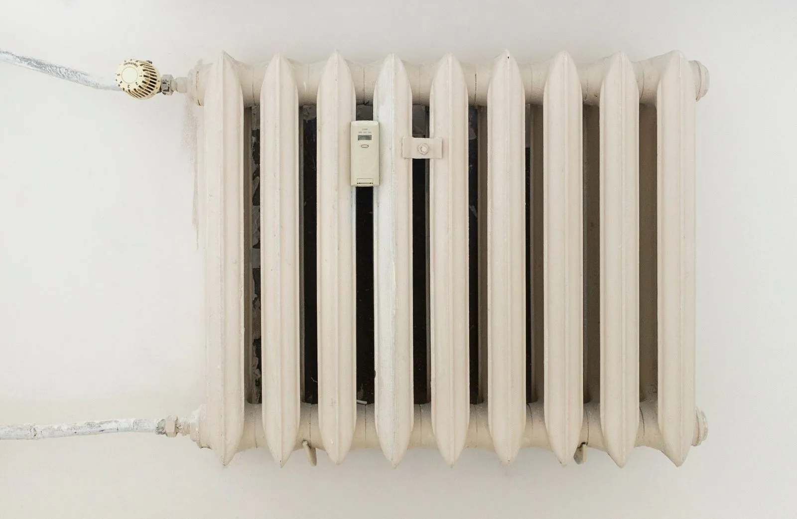 Heizkörper und Lüftungsgitter reinigen: oft vergessen im Leistungsverzeichnis Weiß gestrichener Gussheizkörper mit Thermostatkopf an einer hellen Wand