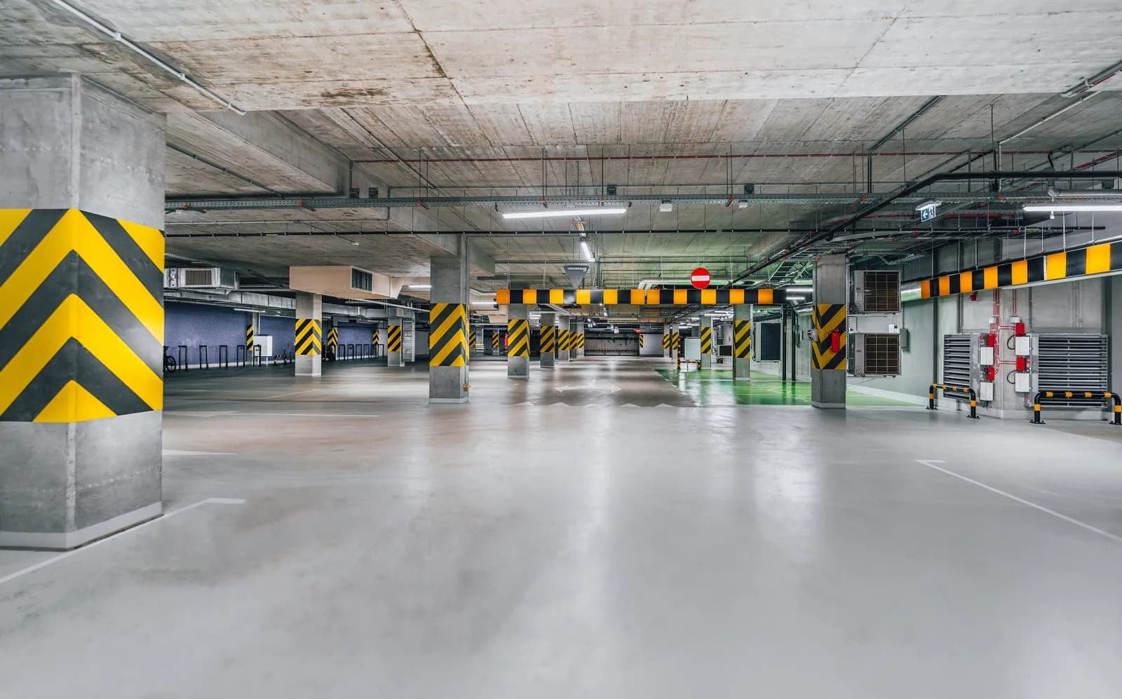 Tiefgarage reinigen: Turnus, Ölflecken und Nebenkosten Menschenleere Tiefgarage mit hellem Betonboden und gelb-schwarz gestreiften Stützpfeilern