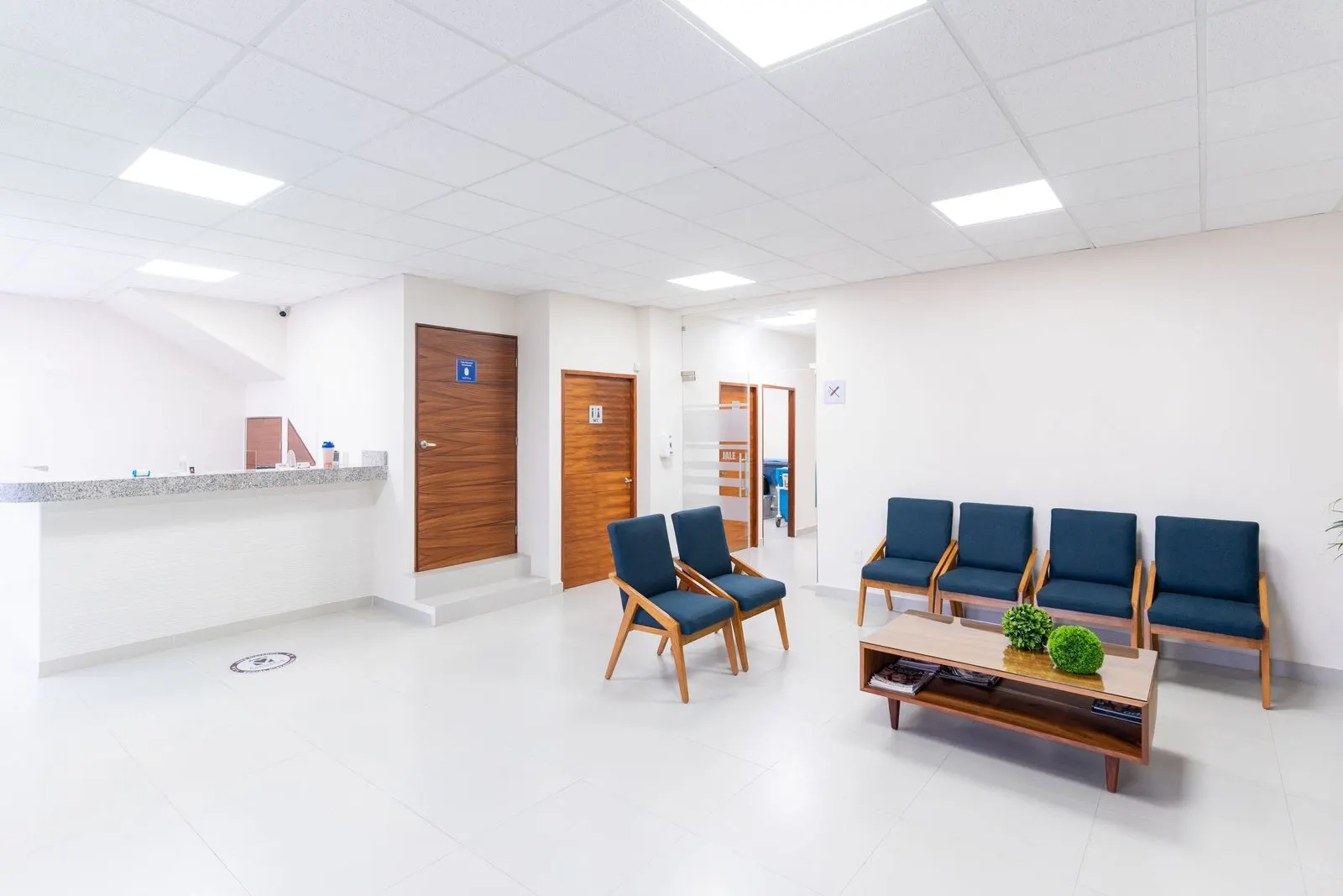 Wartezimmer sauber halten: was Patienten sofort sehen Helles Wartezimmer einer Praxis mit blauen Stühlen, niedrigem Holztisch, Empfangstresen und hellem Fliesenboden